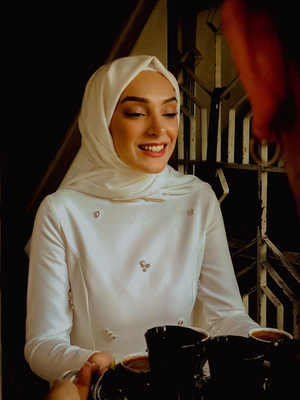 Potret wanita bertudung putih tersenyum sambil menikmati kopi