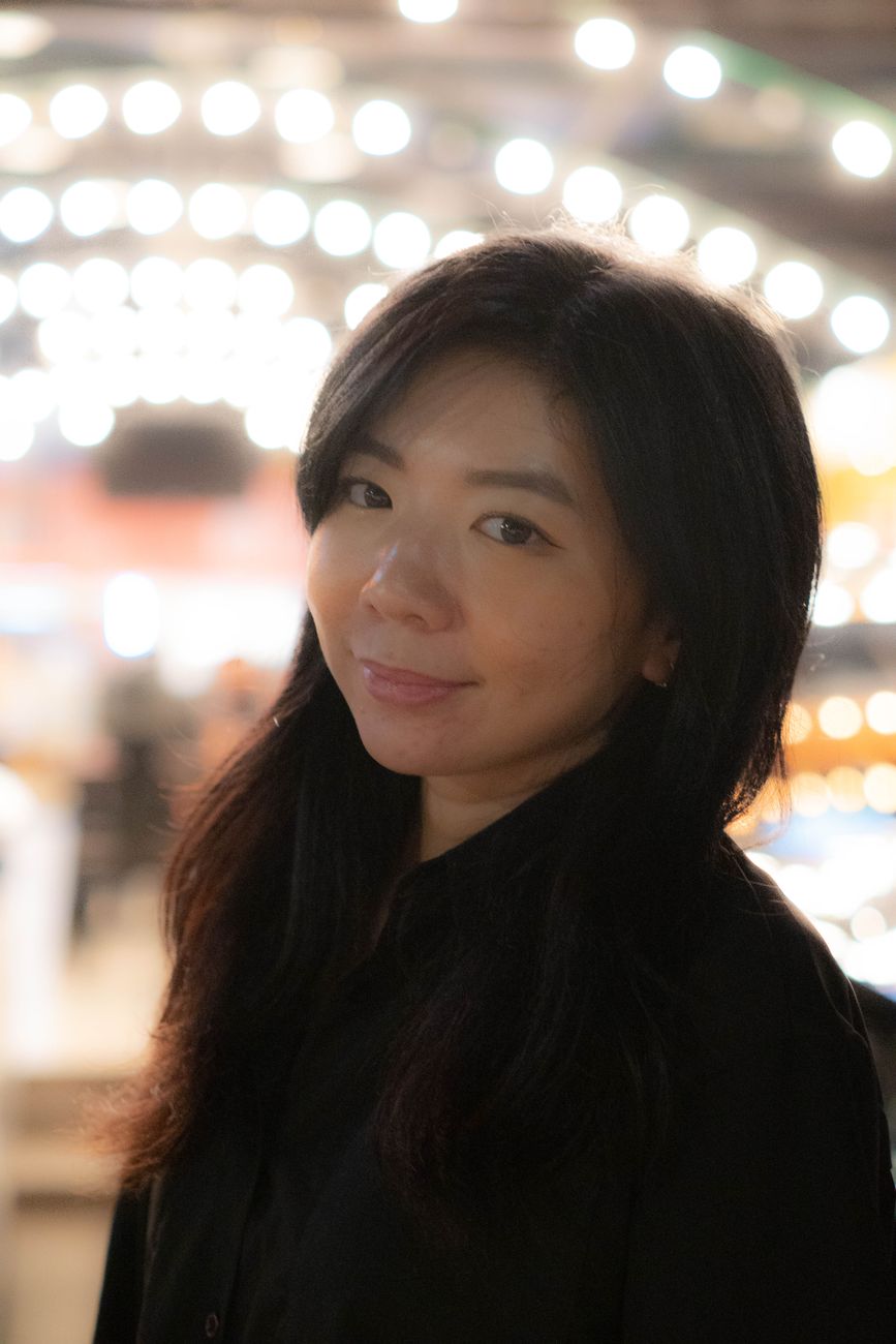 Wanita tersenyum lembut dengan cahaya bokeh di belakang